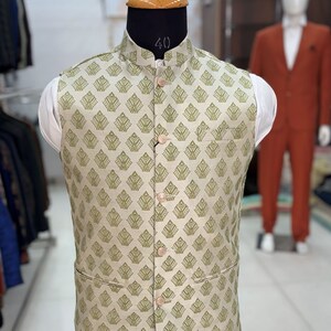 May include: A beige sleeveless waistcoat with a green geometric pattern. The waistcoat has a mandarin collar and four buttons down the front.