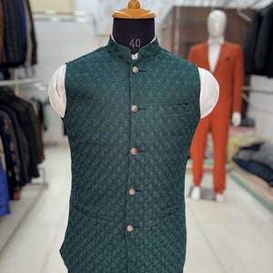 May include: A dark green waistcoat with a textured pattern and button closures. The waistcoat has a mandarin collar and a pocket on the left side.