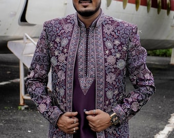 May include: A formal outfit featuring a dark purple jacket and shirt. The jacket is elaborately embroidered with floral and geometric patterns in purple, white, and green. A gold watch with a black strap is visible on the wrist.