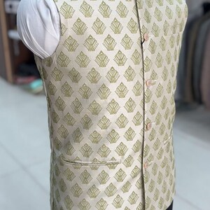 May include: A beige sleeveless waistcoat with a green geometric pattern. The waistcoat has a mandarin collar and a button closure.