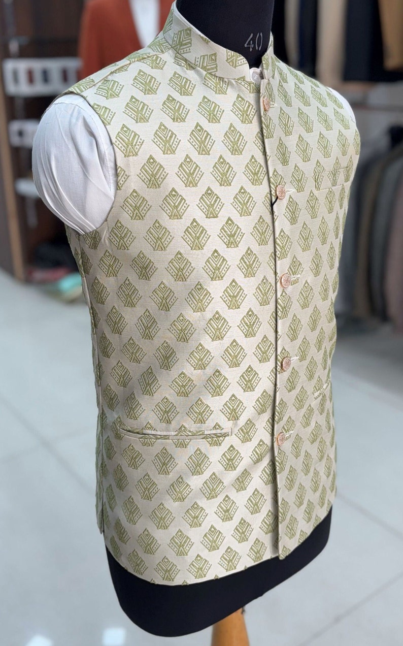 May include: A beige sleeveless waistcoat with a green geometric pattern. The waistcoat has a mandarin collar and a button closure.