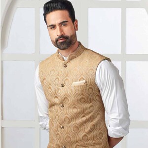 May include: A gold-colored vest with a detailed, repeating pattern. The vest has a mandarin collar and a pocket on the chest. It is worn over a white long-sleeved shirt. The vest's design is reminiscent of a peacock feather.