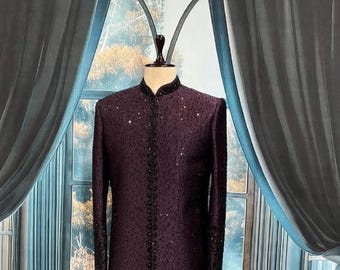 May include: A formal, dark burgundy jacket with a mandarin collar and long sleeves. The jacket is embellished with small, sparkling sequins and black trim along the front and cuffs. The garment is displayed on a mannequin.