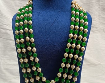 Puede incluir: Un collar de múltiples hilos con cuentas verdes y blancas alternadas. El collar se muestra en un maniquí de terciopelo azul.