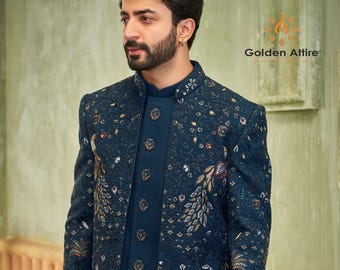 May include: A teal blue men's jacket with a mandarin collar and intricate embroidery featuring peacocks and floral designs. The jacket has a button closure and is made of a luxurious fabric. The text "Golden Attire" is visible in the upper right corner of the image.