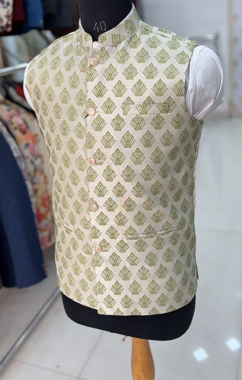 May include: A beige sleeveless waistcoat with a green geometric pattern. The waistcoat has a mandarin collar and four buttons down the front.