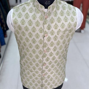 May include: A beige sleeveless waistcoat with a green geometric pattern and button fastenings. The waistcoat has a mandarin collar and a pocket on the left side.