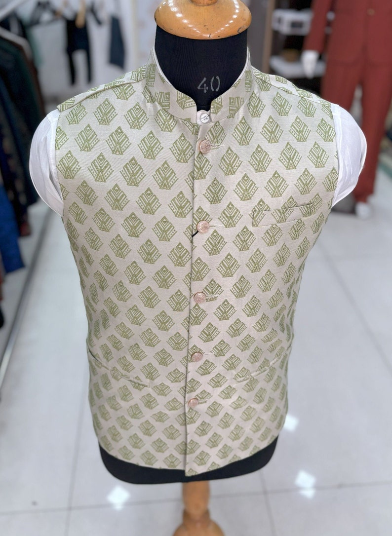 May include: A beige sleeveless waistcoat with a green geometric pattern and button fastenings. The waistcoat has a mandarin collar and a pocket on the left side.
