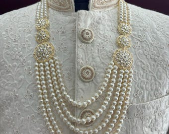 May include: A white pearl necklace with gold accents and a floral design. The necklace has five strands of pearls and three gold pendants with clear stones.