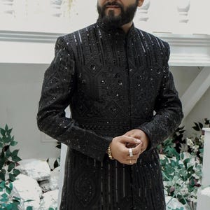K&ouml;nnte beinhalten: Eine schwarze, bestickte Herrenjacke mit Stehkragen und Knopfleiste. Die Jacke hat ein geometrisches Muster und ist aus einem luxuri&ouml;sen Stoff gefertigt.