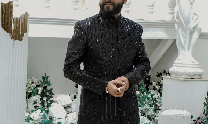 K&ouml;nnte beinhalten: Eine schwarze, bestickte Herrenjacke mit Stehkragen und Knopfleiste. Die Jacke hat ein geometrisches Muster und ist aus einem luxuri&ouml;sen Stoff gefertigt.