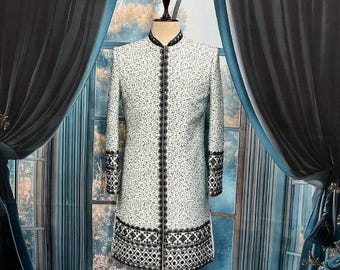 May include: A white and black patterned long coat with a mandarin collar and black trim. The coat features intricate black embroidery along the front, cuffs, and hem. The coat is displayed on a mannequin.