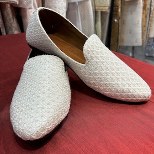 Pode incluir: Um par de sapatos planos brancos bordados com bico fino. Os sapatos t&ecirc;m um brilho sutil e um padr&atilde;o delicado.