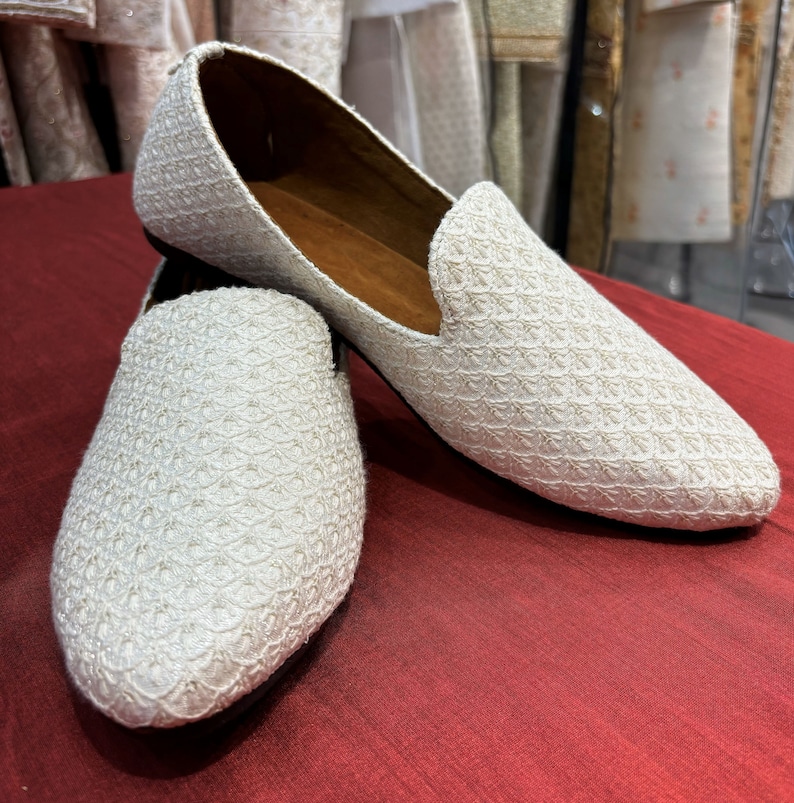 Pode incluir: Um par de sapatos planos brancos bordados com bico fino. Os sapatos t&ecirc;m um brilho sutil e um padr&atilde;o delicado.