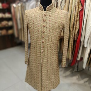 May include: A gold embroidered men's sherwani with a high collar and button closure. The sherwani has a floral pattern and is displayed on a mannequin.