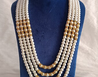 Può includere: Una collana di perle multifilo con accenti dorati. La collana è esposta su un busto di manichino in velluto blu.
