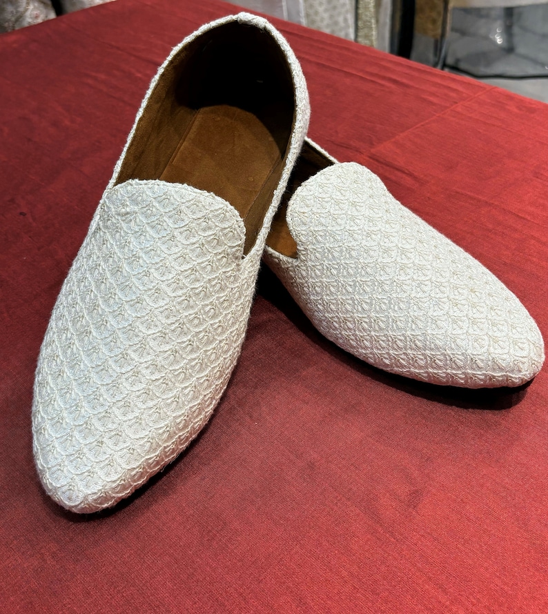 Pode incluir: Um par de mocassins brancos bordados com bico fino. Os mocassins t&ecirc;m um padr&atilde;o sutil e s&atilde;o feitos de um tecido macio e texturizado.