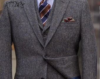 May include: A grey herringbone tweed suit jacket with a blue and brown striped tie and a patterned pocket square. The jacket has a three-button closure and a single vent at the back.