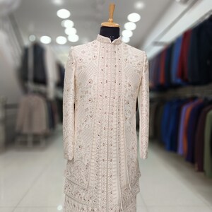 Puede incluir: Una kurta blanca bordada para hombre con cuello alto y detalles intrincados. La kurta est&aacute; en un maniqu&iacute; y tiene un dise&ntilde;o largo y fluido. La tela es un material ligero y transparente. La kurta es una prenda tradicional india.