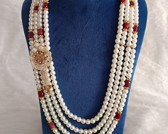 Può includere: Una collana di perle multifilo con accenti rossi e dorati. La collana è esposta su un supporto in velluto blu.