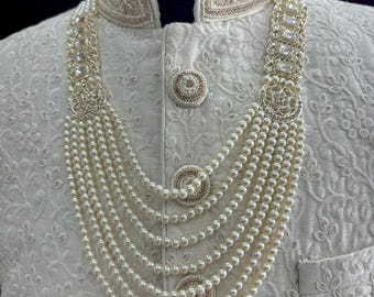 Può includere: Una collana di perle bianche e cristalli con un design decorativo. La collana è composta da più file di perle e presenta un grande ciondolo di cristallo.