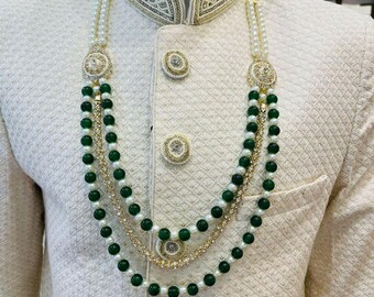 Puede incluir: Un collar de tres hileras con cuentas verdes y detalles dorados. El collar tiene un gran colgante adornado con piedras blancas.