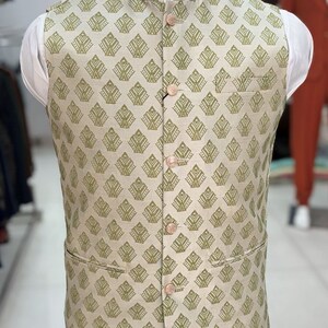 May include: A beige waistcoat with a green geometric pattern and five buttons. The waistcoat has a mandarin collar and two pockets.