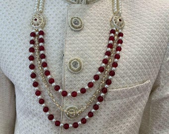 May include: A white and gold beaded necklace with red beads. The necklace has a decorative pendant with gold and white stones.