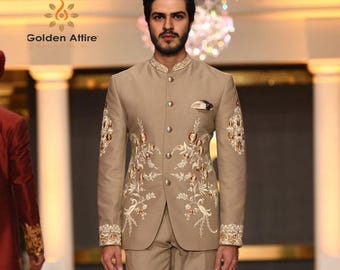 May include: A tan suit with intricate floral embroidery. The suit features a mandarin collar, a pocket square, and decorative buttons. The embroidery is in shades of gold and white. The suit is part of the Golden Attire collection.