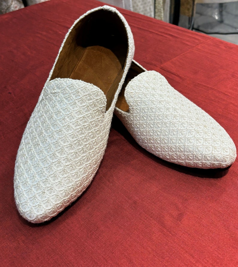Pode incluir: Um par de mocassins brancos bordados com bico fino. Os mocassins t&ecirc;m um padr&atilde;o sutil e s&atilde;o feitos de um tecido macio e texturizado.