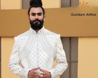 Puede incluir: Chaqueta crema bordada con un cuello alto. La chaqueta presenta patrones detallados y pequeños acentos rojos. El texto "Golden Attire" es visible. La persona lleva la chaqueta.