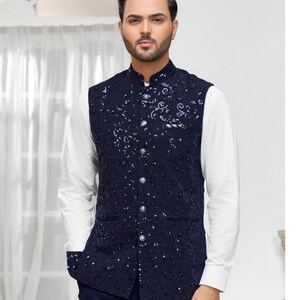 May include: A navy blue waistcoat with a white shirt underneath. The waistcoat has a floral pattern and is adorned with silver buttons.