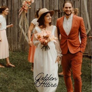 Può includere: Una coppia in abito da sposa. La sposa indossa un abito bianco e un cappello, con un bouquet. Lo sposo indossa un abito color ruggine. Lo sfondo include una staccionata di legno e decorazioni floreali. Il testo "Golden Attire" è visibile.