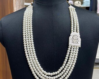 May include: A multi-strand pearl necklace with a decorative silver-colored pendant. The necklace is displayed on a black mannequin. The pendant has an ornate design. The pearls are white and round.