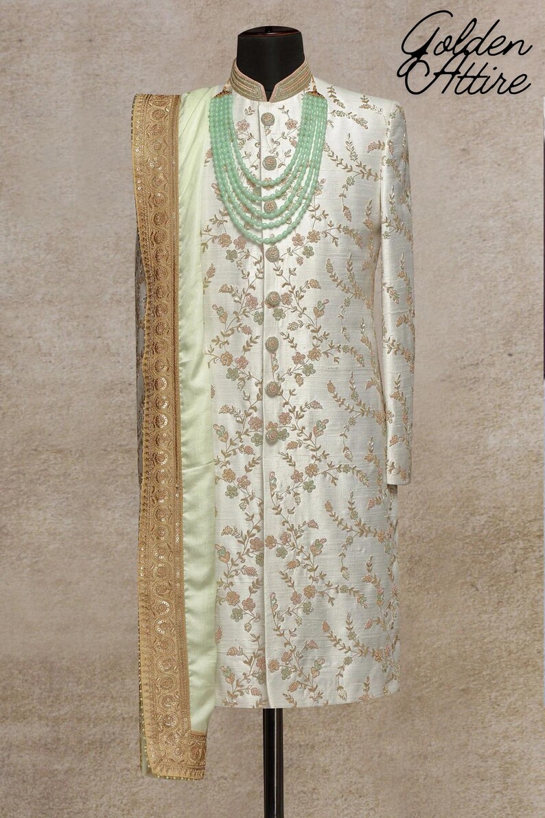 K&ouml;nnte beinhalten: Ein wei&szlig;er Sherwani mit Blumenmuster und ein hellgr&uuml;ner Schal mit goldenen Verzierungen. Der Sherwani hat einen hohen Kragen und einen Knopfverschluss. Eine hellgr&uuml;ne Perlenkette wird &uuml;ber dem Sherwani getragen.