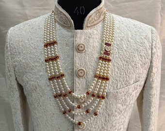 Può includere: Una giacca bianca da uomo ricamata con una collana di perle multifilo con perline rosse. La collana ha una chiusura dorata con una pietra rossa.