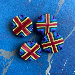 Puede incluir: Cuatro botones redondos con un diseño tejido. Los botones están hechos de hilos coloridos en tonos de rojo, amarillo, azul, verde y morado. Los botones están dispuestos en un semicírculo.