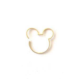 Può includere: Un'intelaiatura dorata a filo della testa di Mickey Mouse, con due grandi orecchie circolari e una forma della testa arrotondata. Il design è semplice e minimalista, su uno sfondo bianco.