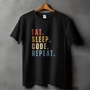 Op de afbeelding: Zwart T-shirt met een vintage-stijl grafische afbeelding met de tekst "Eat. Sleep. Code. Repeat."