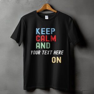 May include: Black t-shirt with a vintage-style graphic that says "Keep Calm and [Your Text Here] On". The text is in different colors, including blue, red, green, and yellow.