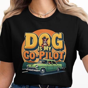 May include: Black t-shirt with a graphic design. The design features the text "DOG IS MY CO-PILOT", a dog, and a vintage green car. The background is an orange and yellow circle, evoking a retro style.