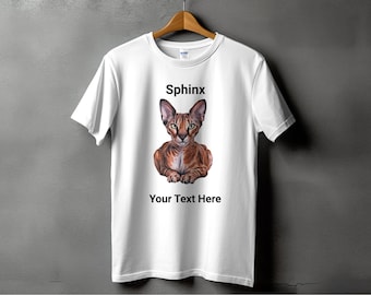 以下が含まれることがあります： スフィンクスの猫がプリントされた白いTシャツ。猫は茶色と白で、真剣な表情をしています。「Sphinx」という文字が猫の上に、「Your Text Here」という文字が猫の下にプリントされています。