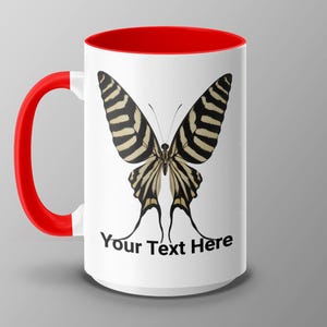 May include: White ceramic mug with a red rim and handle. The mug features a black and white butterfly illustration and the text "Your Text Here".