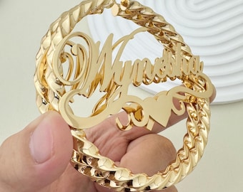 Op de afbeelding: Gouden creolen met de naam "Mynetha" en een hartbedel. De oorbellen zijn gedraaid en hebben een dik, touwachtig ontwerp.