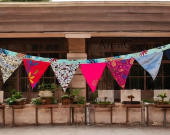 May include: A colorful fabric bunting with triangular flags hangs above a storefront. The flags are decorated with various patterns and colors, including blue, red, yellow, and green. The storefront has a brown wooden facade and a sign that reads "Artist Centre".