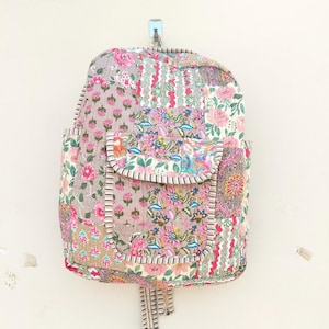 Puede incluir: Una mochila de patchwork con estampado floral en tonos rosa, verde y marrón. La mochila tiene un bolsillo frontal grande y un cierre de cordón.