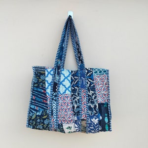 Puede incluir: Una bolsa de mano azul y blanca de patchwork con un diseño acolchado. La bolsa tiene dos asas y está colgada de un gancho.