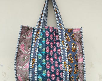 Könnte beinhalten: Eine gesteppte Tragetasche mit Patchwork-Design. Die Tasche zeigt Paisley- und Blumenmuster in Rosa, Blau, Braun und Orange. Die Griffe und Kanten sind mit einem gestreiften Stoff verziert.