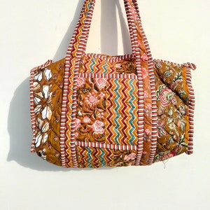 Puede incluir: Un bolso tote acolchado marrón con estampados florales y geométricos. El bolso tiene dos asas largas y un diseño de patchwork.