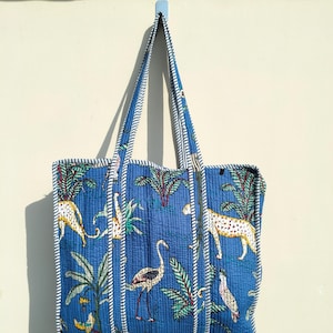 May include: A blue quilted tote bag with white stripes and a white trim. The bag features a tropical print with leopards, birds, and palm trees.